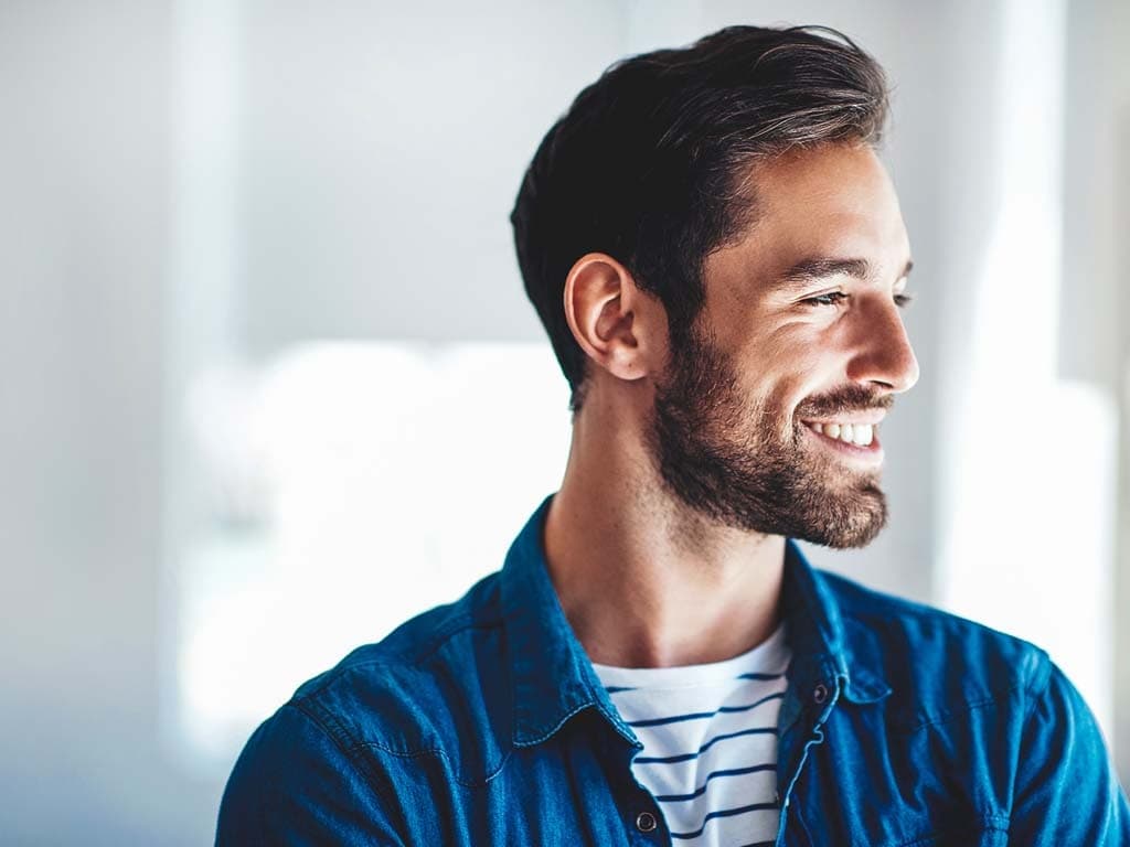 Un bărbat zâmbitor cu barbă, purtând o cămașă albastră, emanând o atitudine prietenoasă și accesibilă