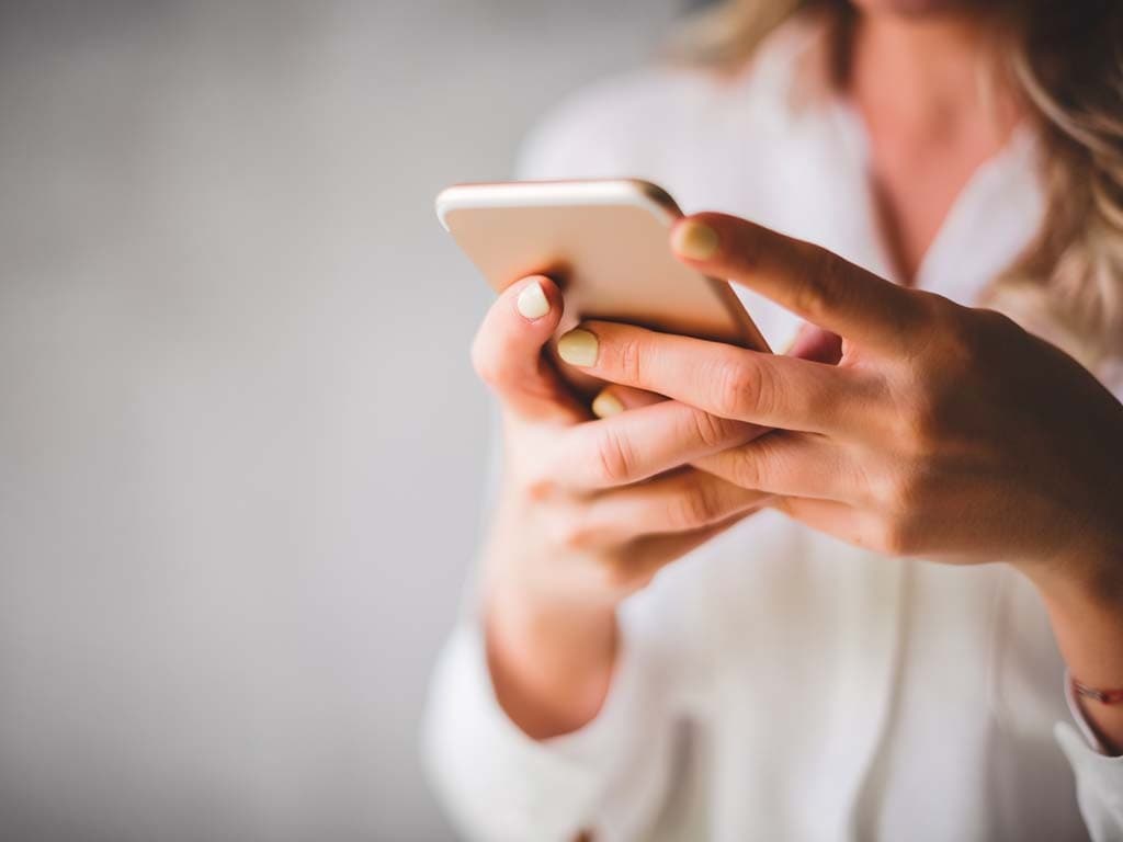 O femeie ține un telefon mobil în mână, fiind implicată într-o conversație sau răsfoind conținut pe dispozitiv