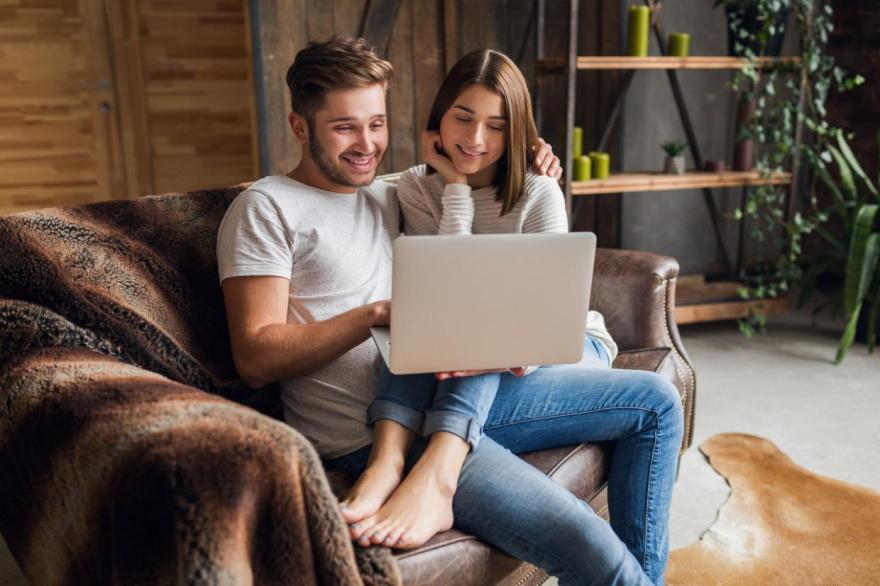 Young smiling couple sitting couch home casual outfit love romance woman man embracing wearing jeans spending relaxing time together holding laptop Easy Resizecom 