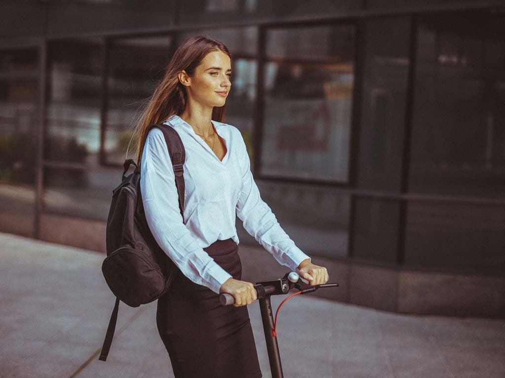 O femeie în costum de afaceri se deplasează pe trotinetă, arătând o combinație între profesionalism și mobilitate modernă