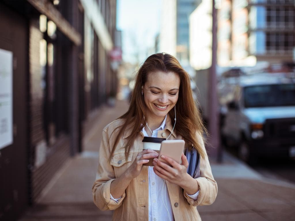 O femeie ține o ceașcă de cafea și privește telefonul, părând concentrată și implicată în ceea ce face