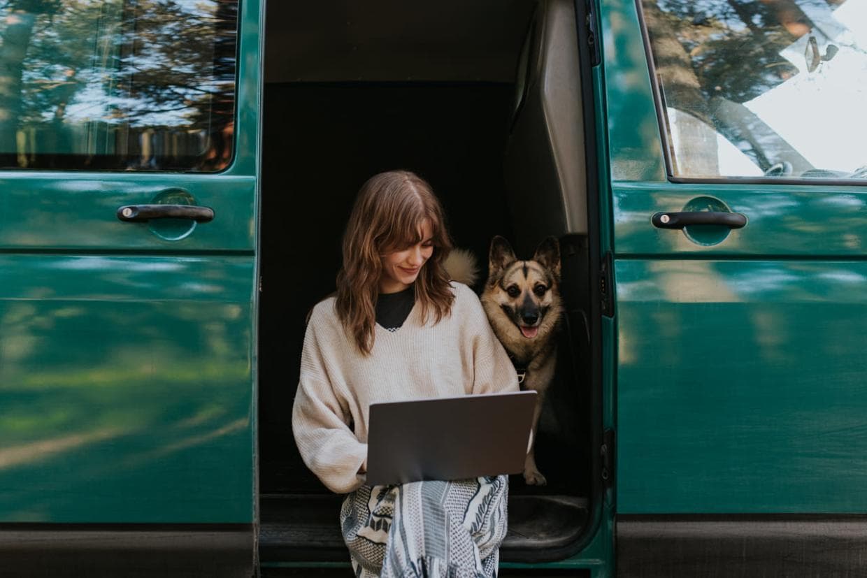 O femeie stă într-o rulotă cu un câine care se odihnește confortabil în poala ei, amândoi părând relaxați și mulțumiți