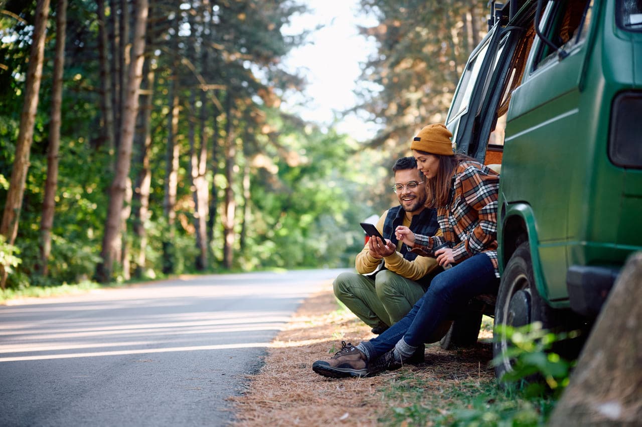 Two people sitting on a van's side, focused on a tablet, sharing information or enjoying a moment together