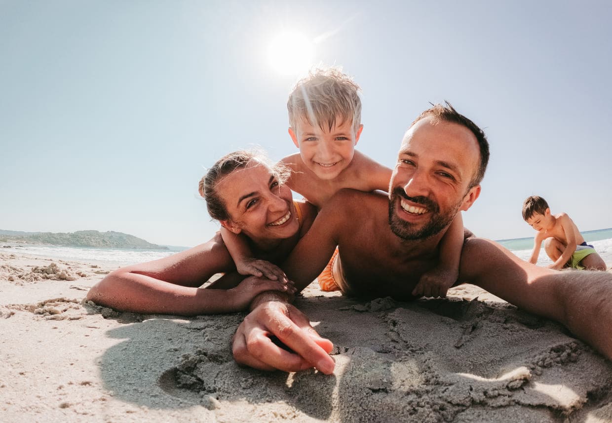 O familie fericită se joacă împreună pe plajă, zâmbind și bucurându-se de o zi însorită lângă ocean
