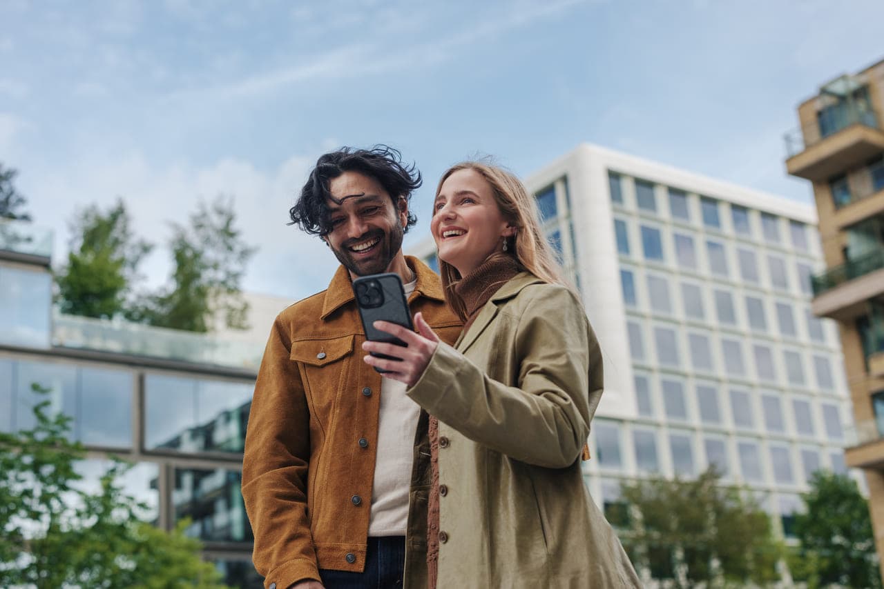 Un bărbat și o femeie zâmbesc în timp ce își fac un selfie în fața unei clădiri moderne