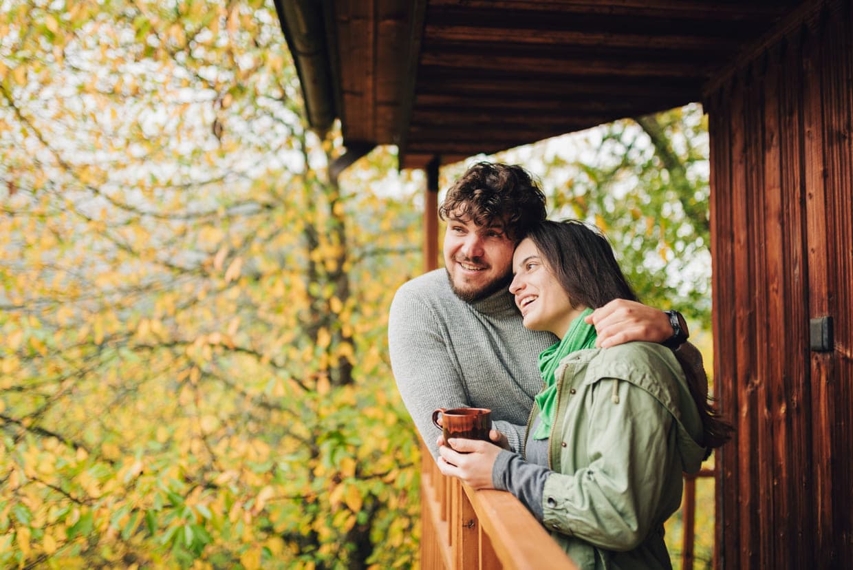 Un cuplu se bucură de un moment cozy pe un balcon înconjurat de frunziș vibrant de toamnă
