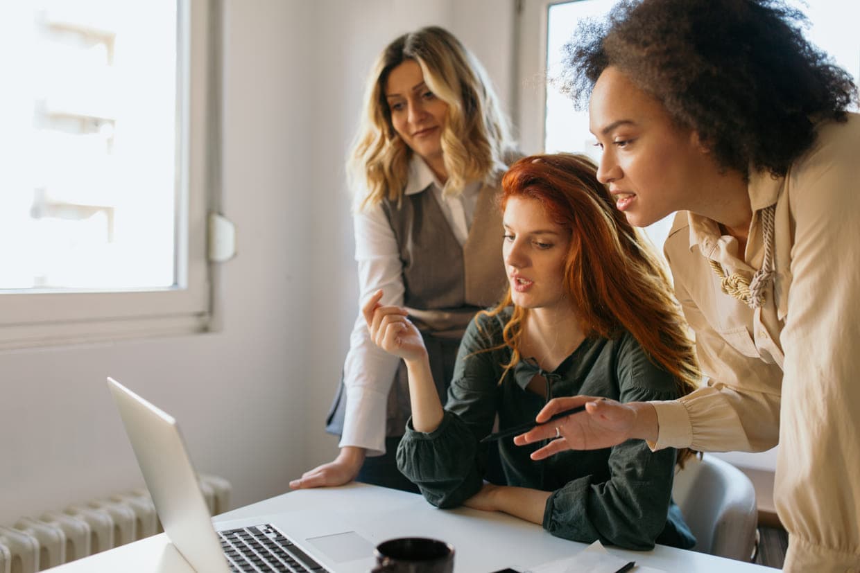 Un grup de trei femei examinează un laptop, colaborând și discutând informațiile afișate